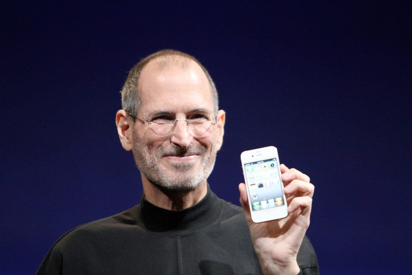 Steve Jobs, sorrindo, segura um iPhone 4 branco.