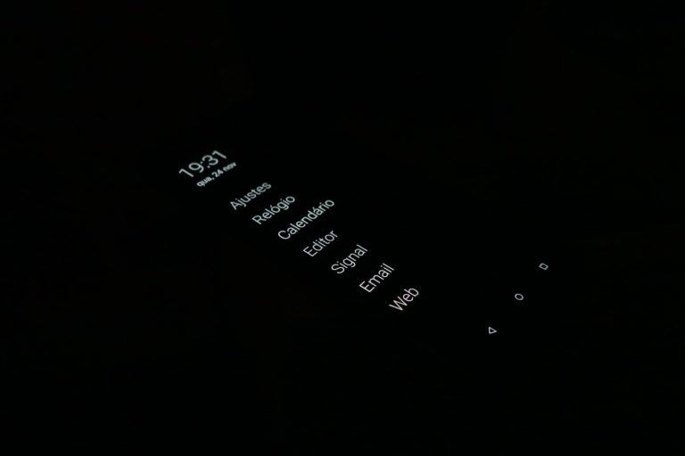 Foto do celular no escuro total. Vê-se apenas letras brancas do Olauncher, como se estivessem flutuando.