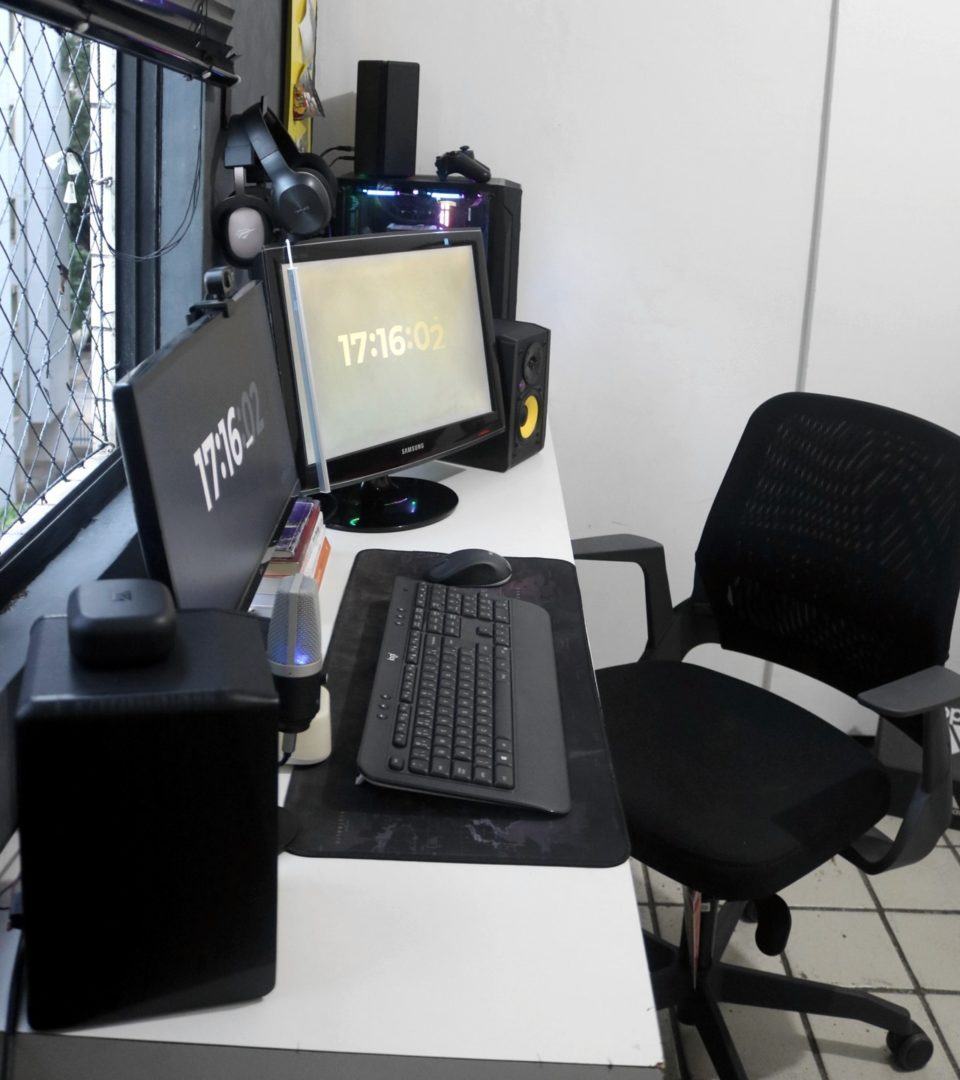 Foto por outro ângulo, lateral, do escritório do Thiago Azevedo, desta vez mostrando a cadeira preta dele.