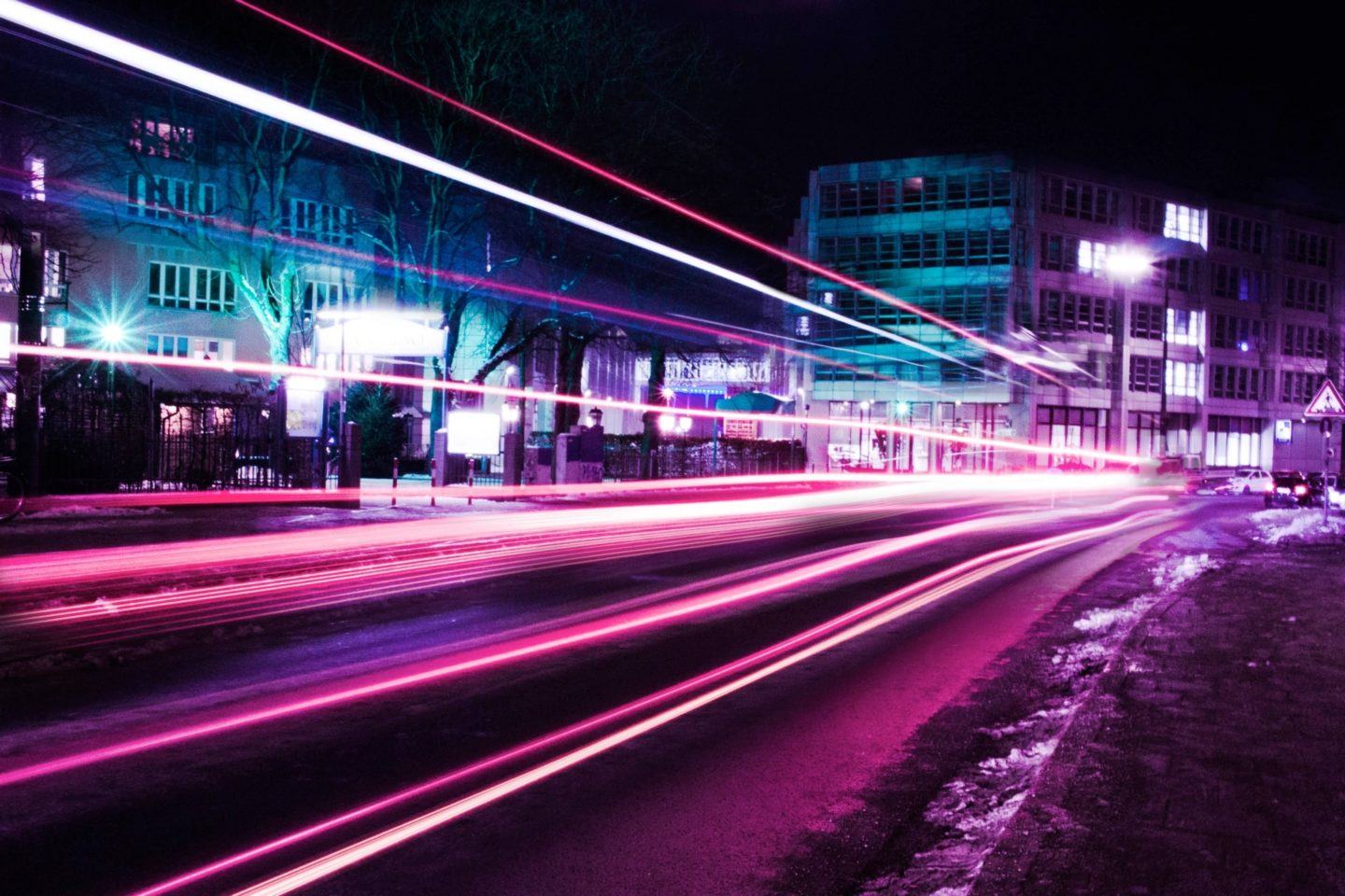 Foto em longa exposição de luzes numa rua, com tons em neon, violeta e verde.