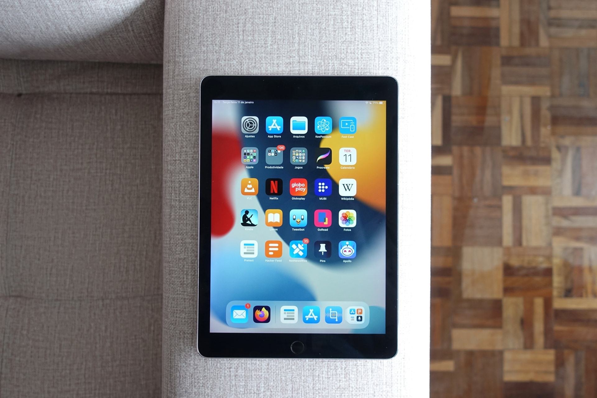 Foto de cima de um iPad Pro sobre um braço de sofá, mostrando o assento à esquerda e um chão de taco à direita.
