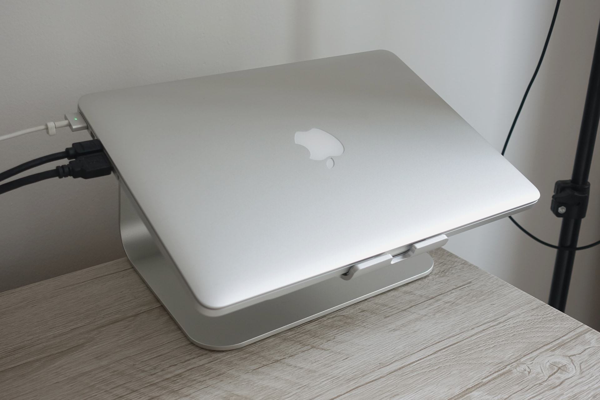 Foto de um MacBook Pro (2015) em um suporte metálico com três cabos conectados do lado esquerdo. Ao fundo, parte de um tripé.