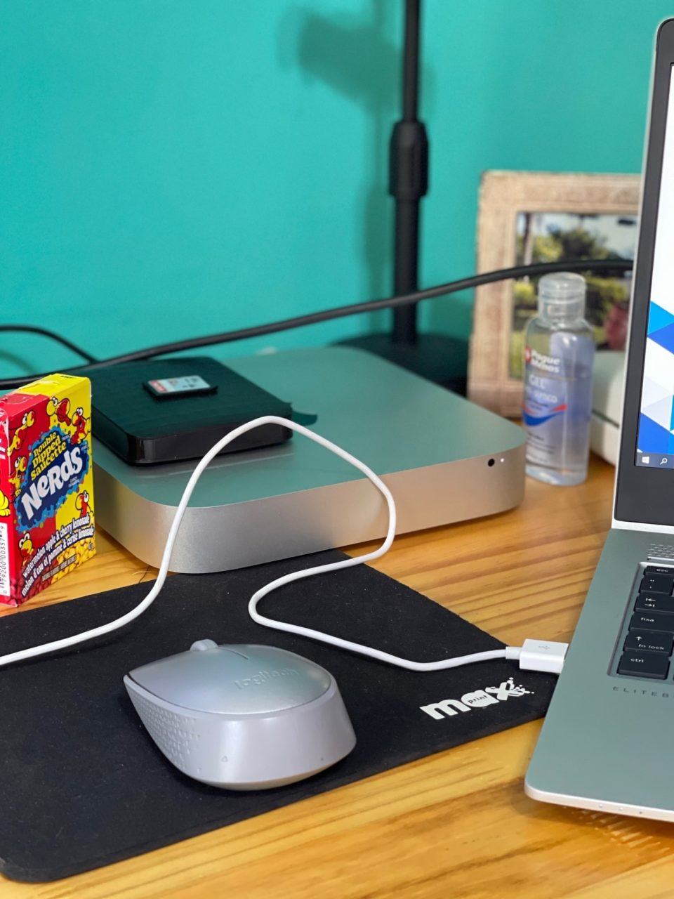 Detalhe da mesa do Jorge, mostrando o mouse, Mac mini com um HD externo em cima, balinhas Nerds, e um peçado do notebook.