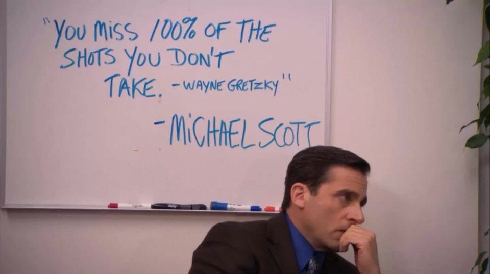 Personagem Michael Scott, the “The Office”, com a mão no queixo e olhando para o lado. Ao fundo, uma lousa branca com a frase (em inglês): “Você erra 100% dos chutes que não dá. — Wayne Gretzky — Michael Scott”