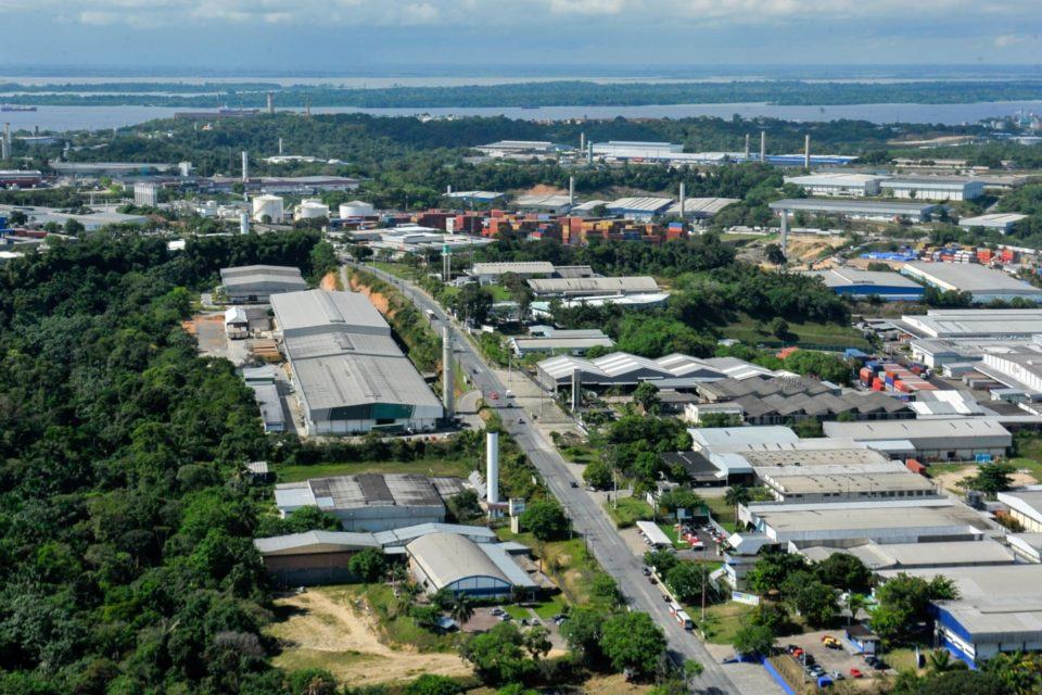Foto aérea do pólo industrial de Manaus, com vários galpões e fábricas e, ao fundo, um grande rio.