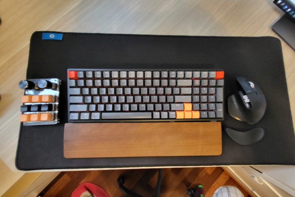 Foto de cima de um teclado mecânico, mouse à direita e teclado minúsculo à esquerda, todos sobre um mousepad enorme, preto.