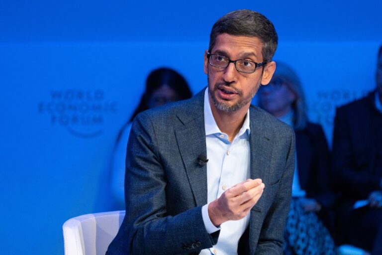 Homem pardo, de óculos de grau, vestindo um paletó e uma camisa azul, gesticula com a mão direita. Ao fundo, painel azul forte com o logo do Fórum Econômico Mundial.
