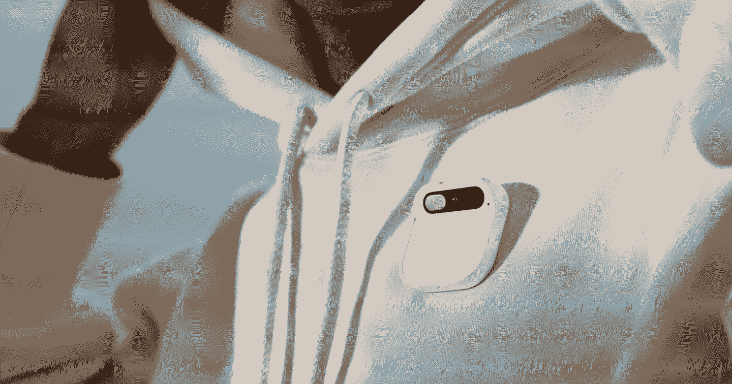 Foto em detalhe do AI Pin, da Humane, grudado a um moletom branco com gorro. Foto tratada com efeito dithering.