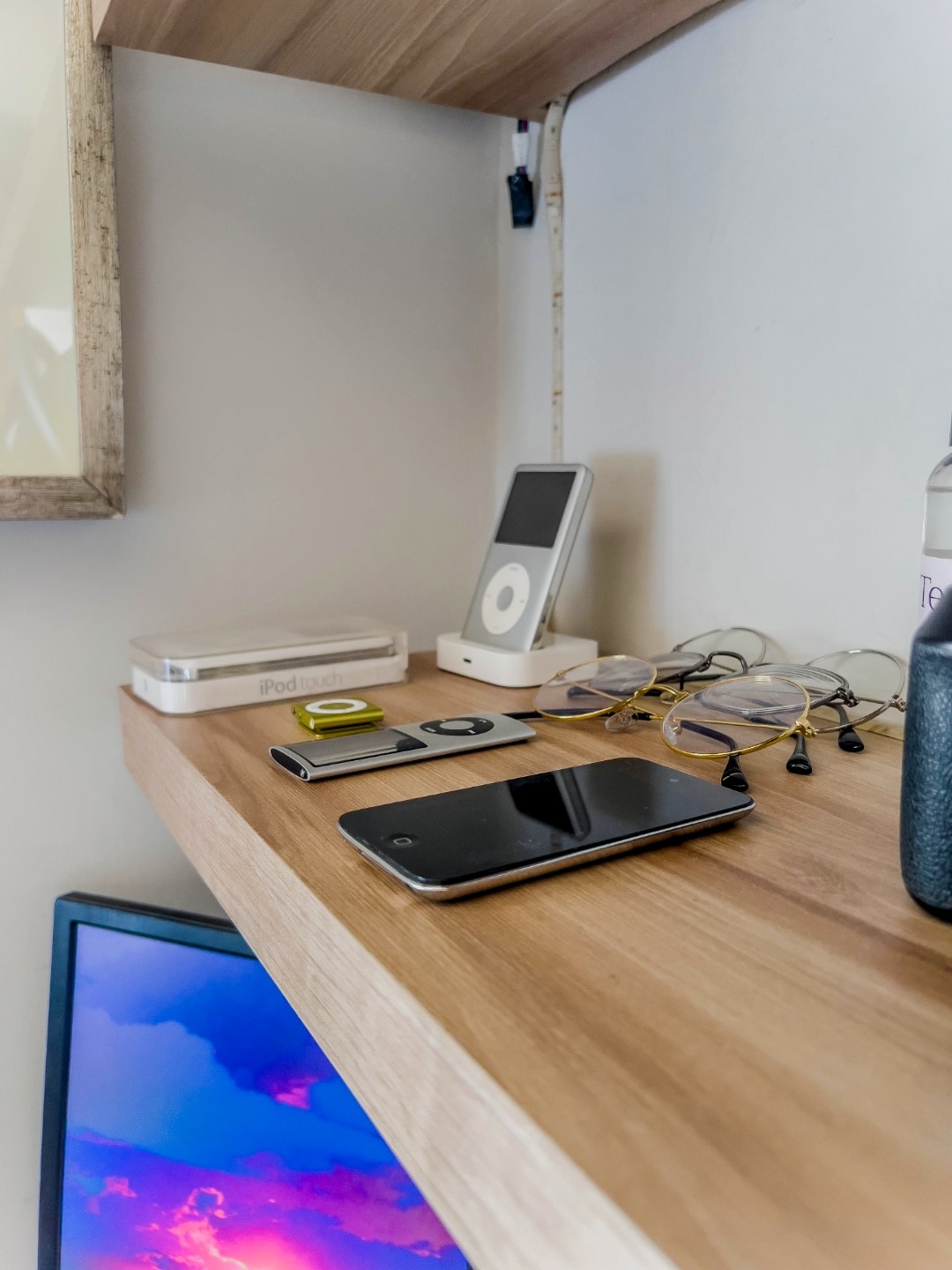 Alguns iPods e óculos de grau sobre uma prateleira de madeira.