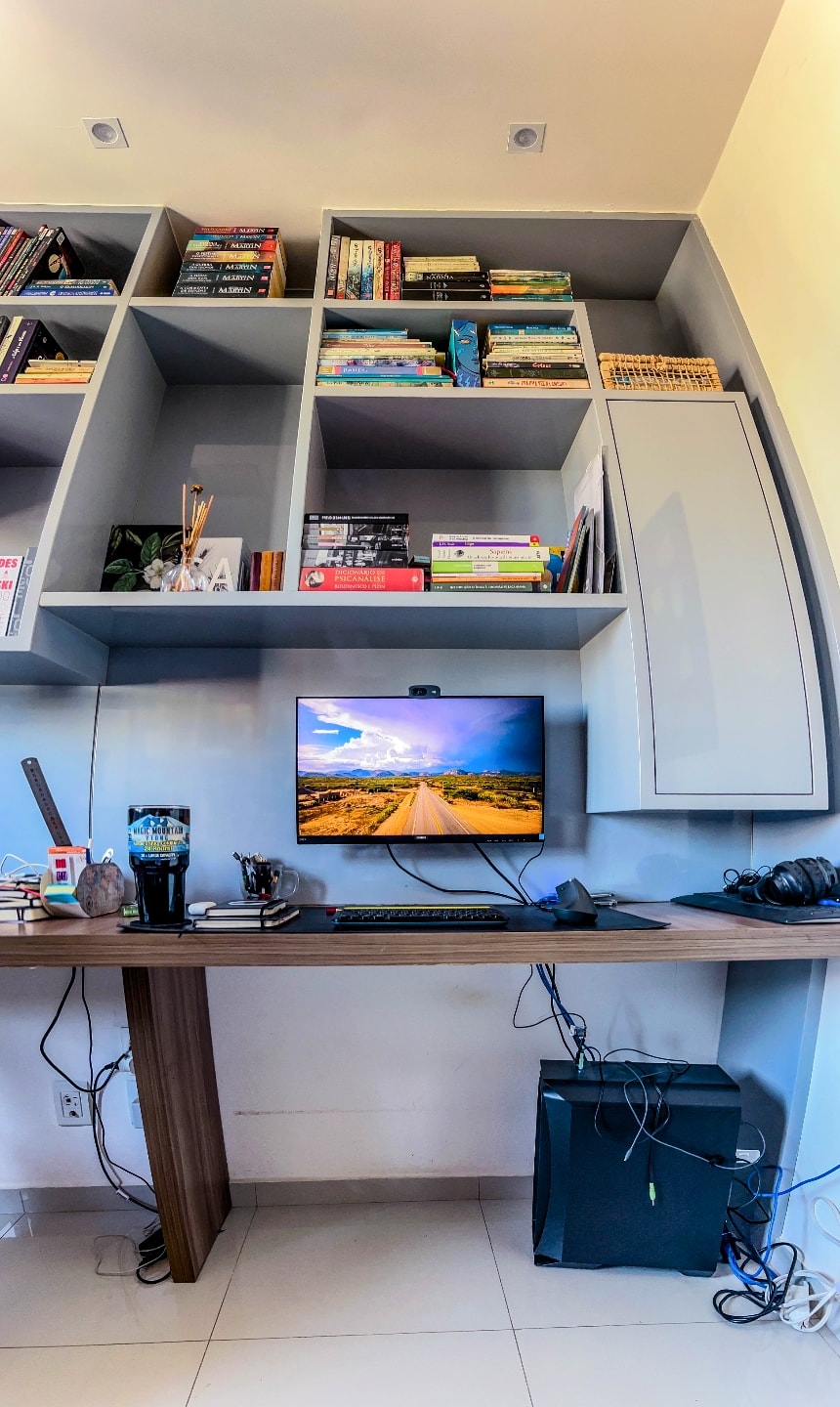 Foto vertical, estilo “olho de peixe”, de toda a mesa, fios e estantes superiores da mesa de trabalho do Caiubi.