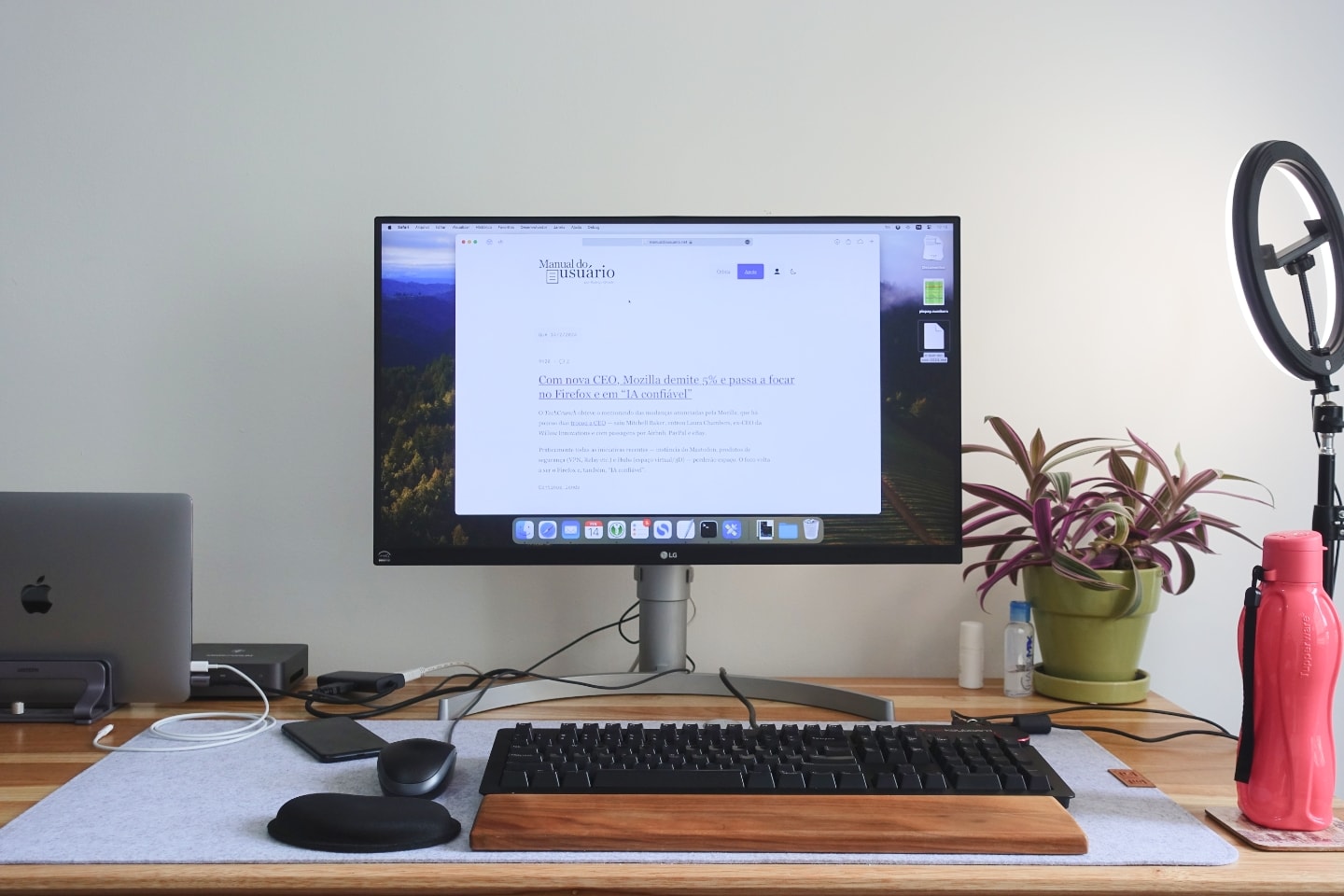 Foto frontal de uma mesa de trabalho, com um monitor grande, acessórios e uma ring light à direita.