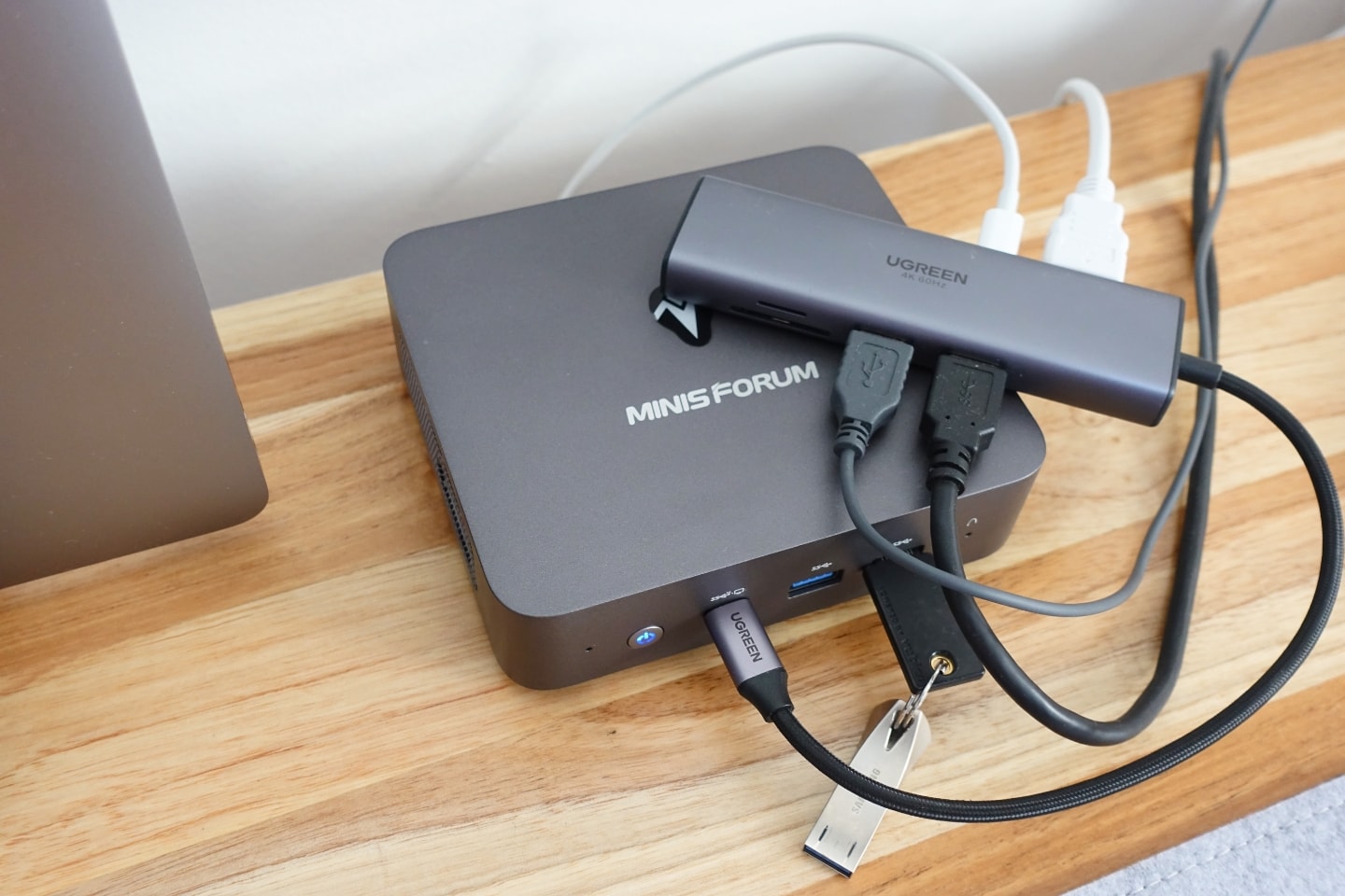 Foto de cima, na diagonal, de um mini PC de metal com um hub USB-C, sobre uma mesa de madeira.