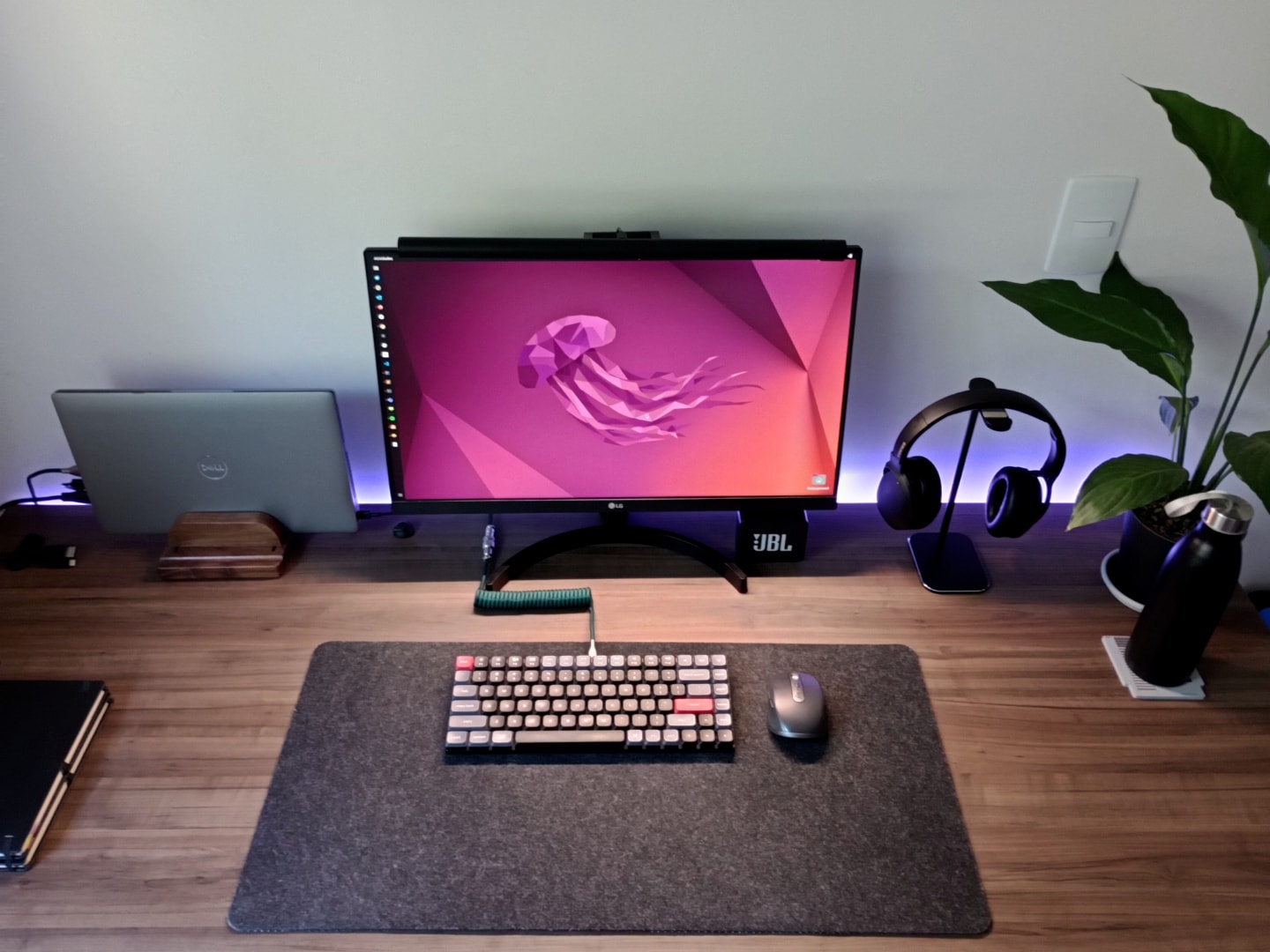 Foto frontal da mesa do Leonardo Santos, com mousepad, teclado e mouse, monitor com papel de parede do Ubuntu e alguns outros itens.