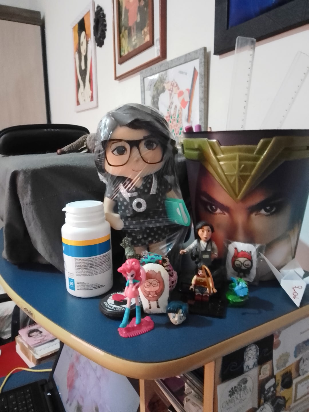 Mesa com alguns bonecos e um balde da Mulher-Maravilha com réguas dentro.
