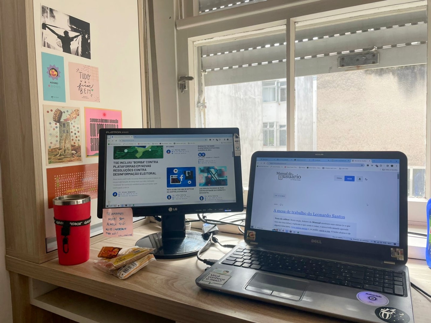 Detalhe do notebook e monitor, com alguns adesivos em uma parede à esquerda.