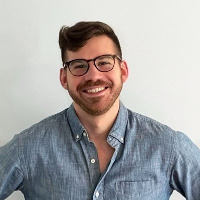 Homem branco, de óculos e barba curta, com camisa jeans.