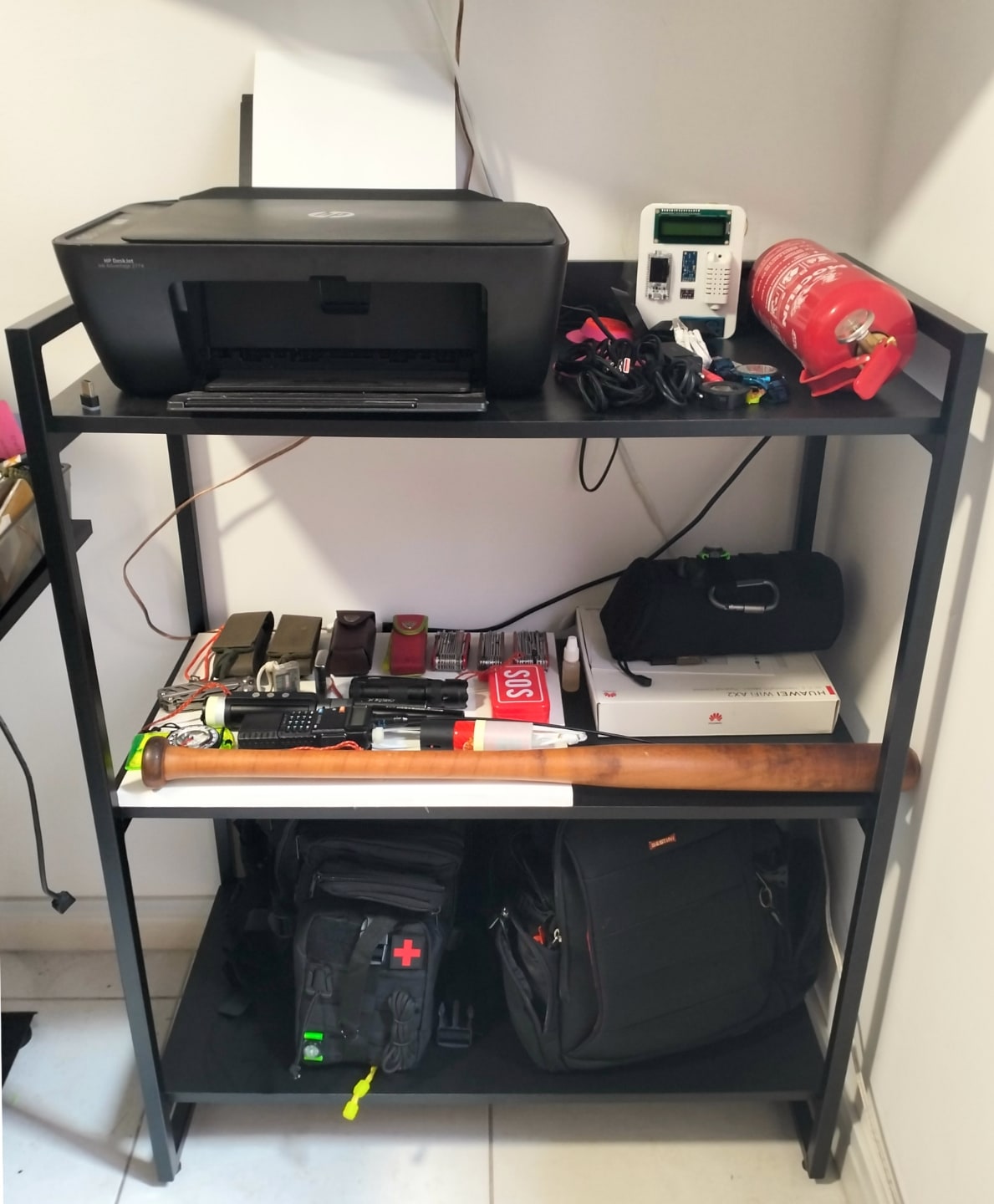 Prateleira com impressora, mochilas e acessórios.
