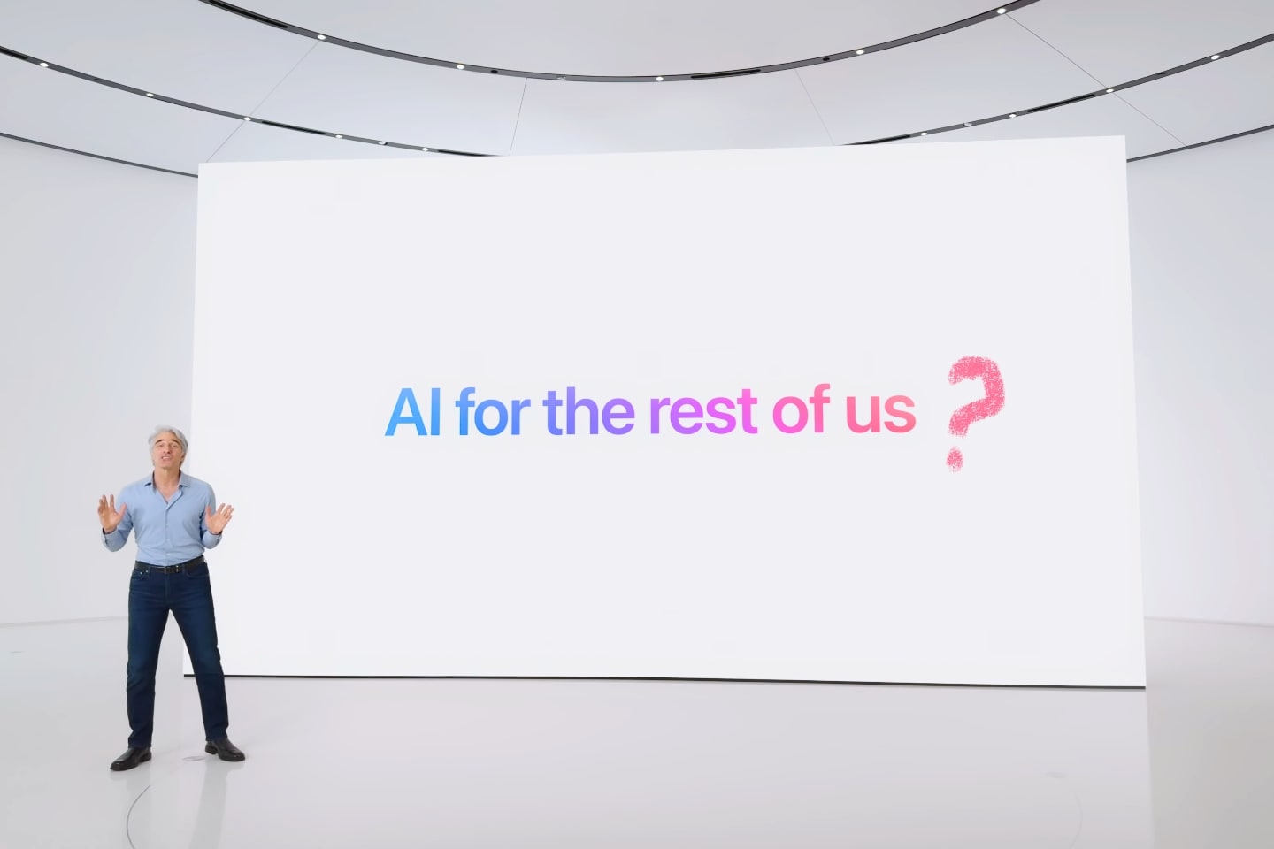 Craig Federighi em frente a um painel branco com a frase “AI for the rest of us” e uma interrogação desenhada/adicionada.