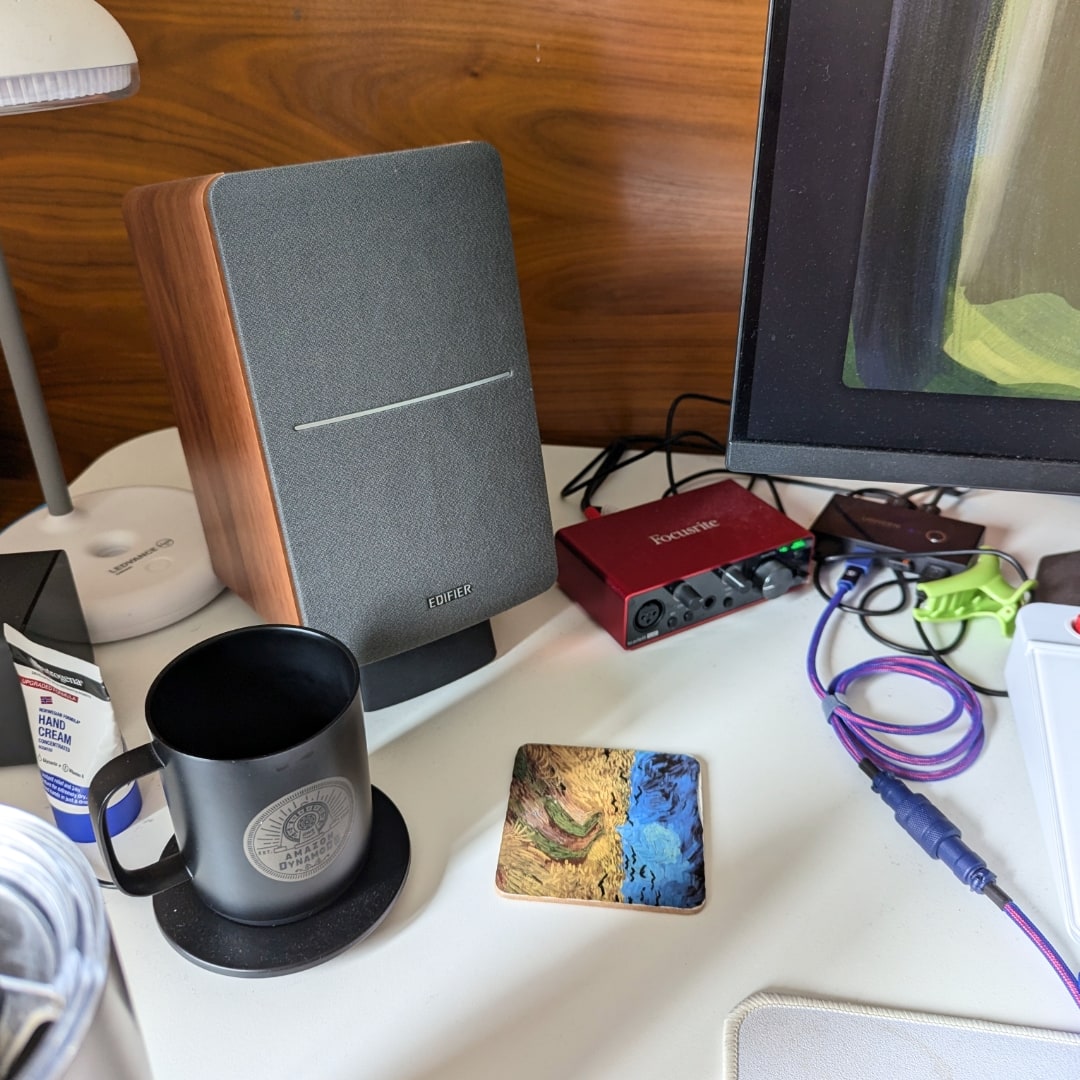 Objetos à esquerda da mesa: caixa de som, caneca e cabos.