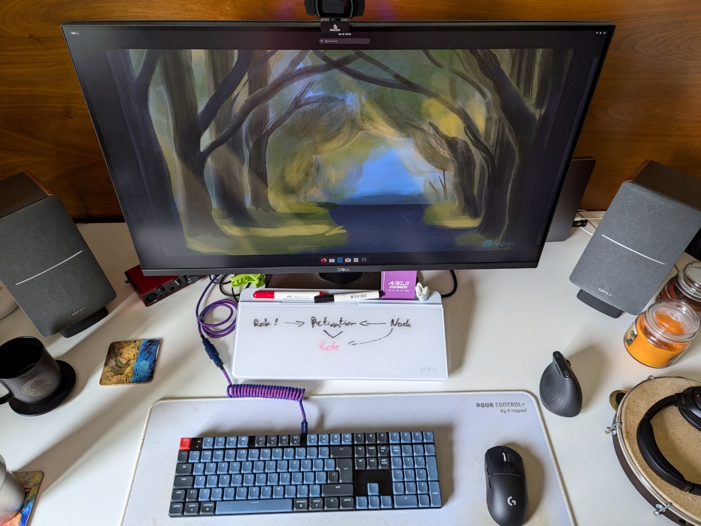 Foto de cima da mesa de trabalho do Raphael, destacando o monitor e acessórios (teclado, mouse e lousa).