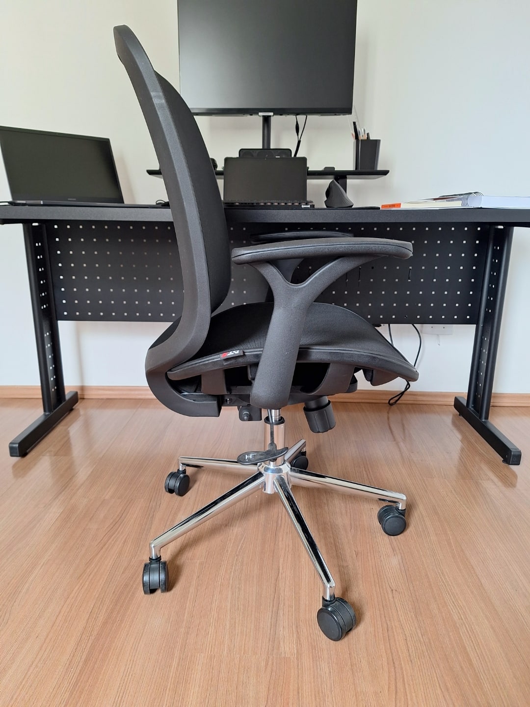 Cadeira de escritório, de perfil, em frente a uma mesa.