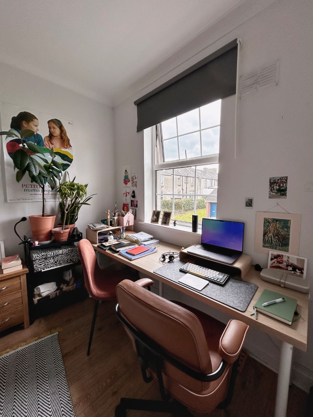 Perspectiva mais ampla, mostrando lado esquerdo da mesa, com outra cadeira, plantas e um pôster na parede.