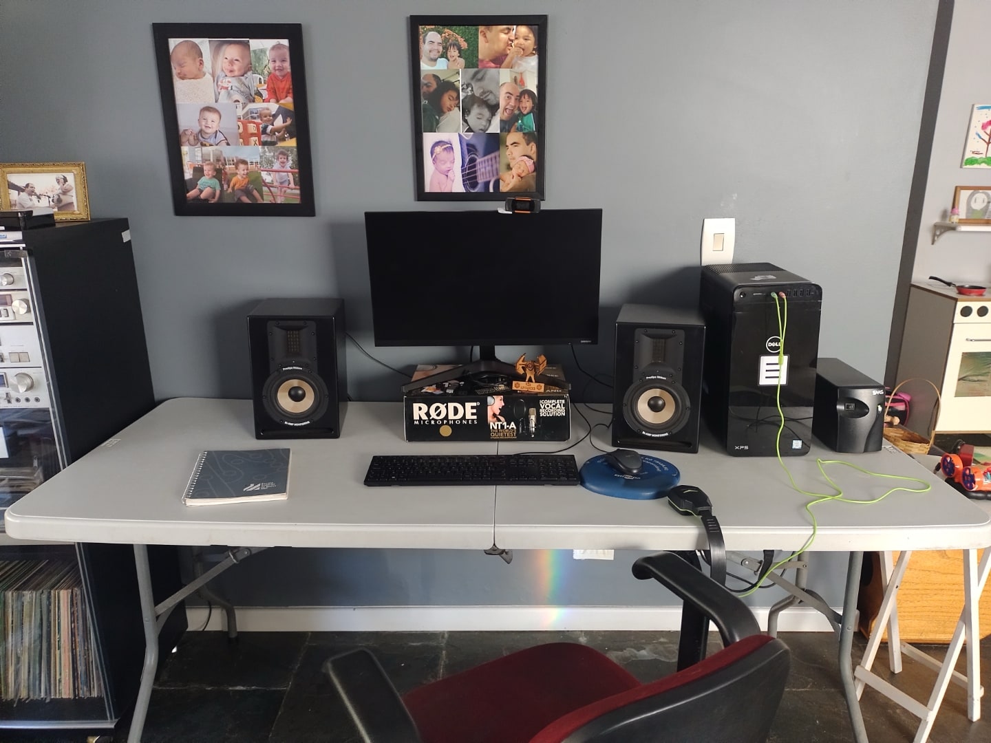 Mesa de trabalho com monitor, duas caixas de som destacadas e quadros com fotos nas paredes.