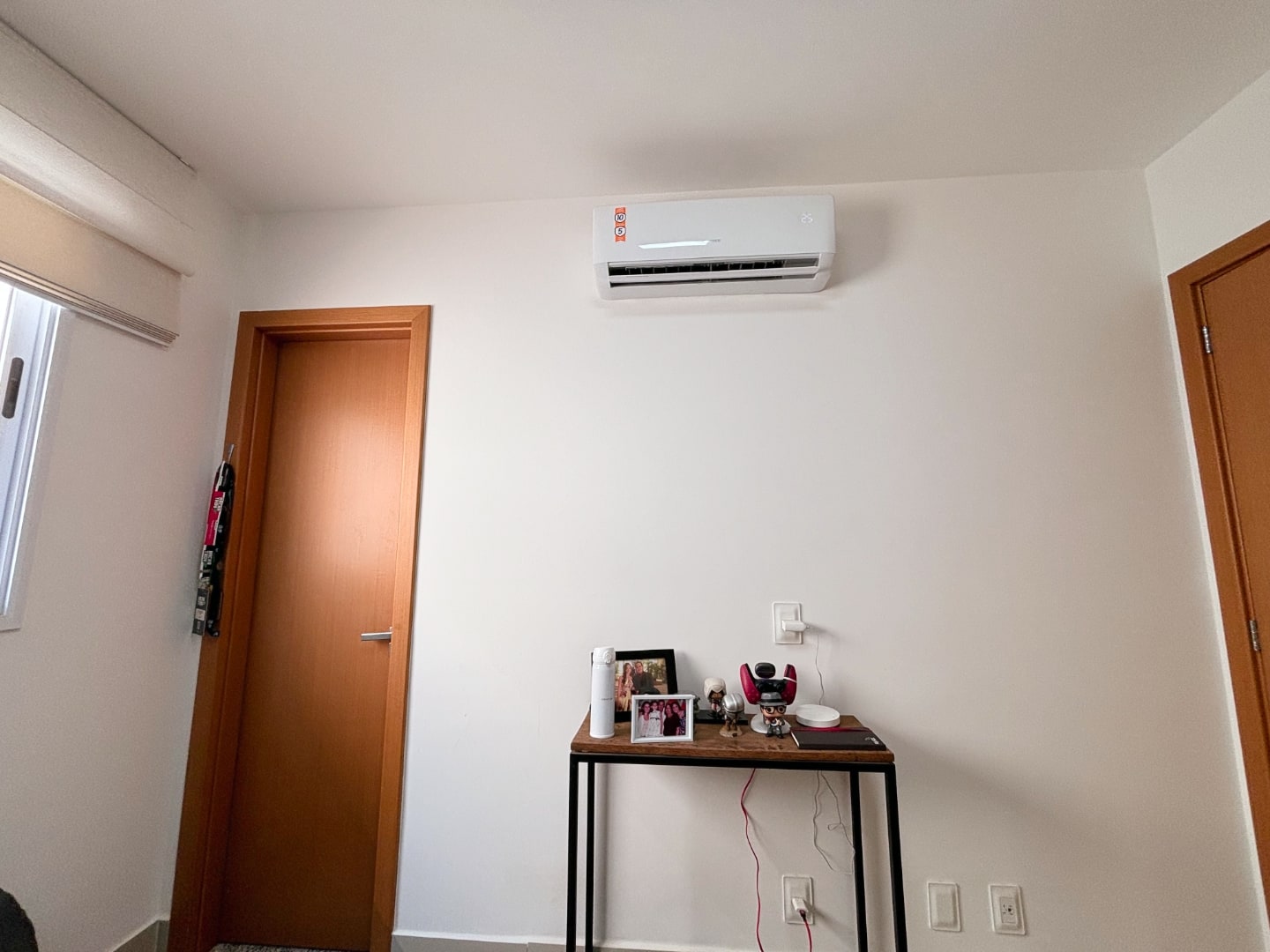 Área atrás da mesa do Vitor, com ar condicionado, duas portas e um aparador curto com alguns bonecos Funko.