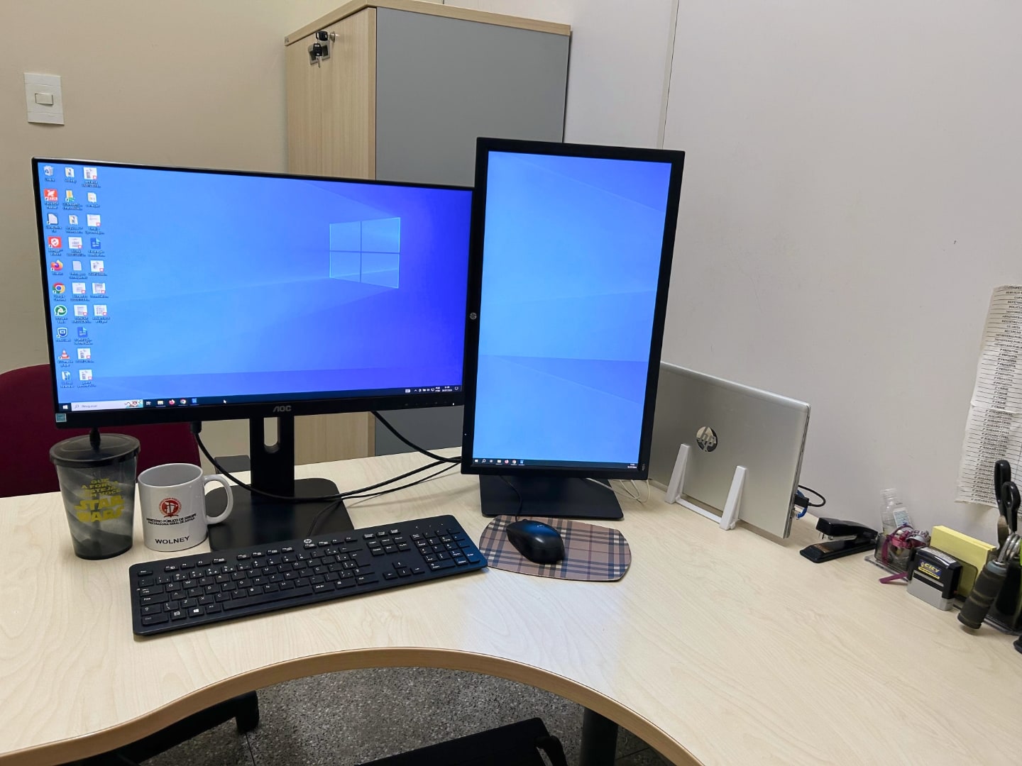 Mesa em “L” com dois monitores, um na vertical, outro na horizontal, exibindo papel de parede do Windows 10.