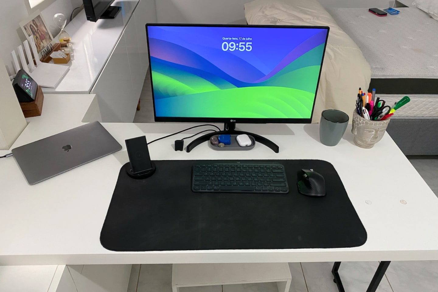 Foto frontal da mesa do Felipe, com monitor, MacBook Air do lado esquerdo e acessórios sobre um deskpad grande.
