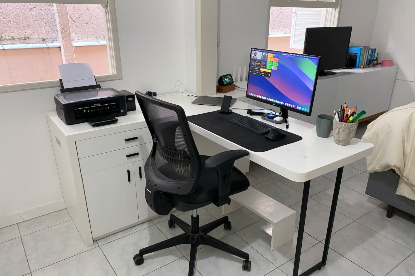 Foto diagonal mostrando a mesa em “L” com computador e impressora, e uma cadeira preta.