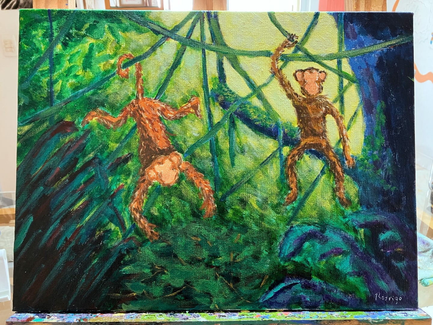 Dois macaquinhos no meio da floresta, um pendurado pelo rabo em um cipó, outro sentado em um galho.