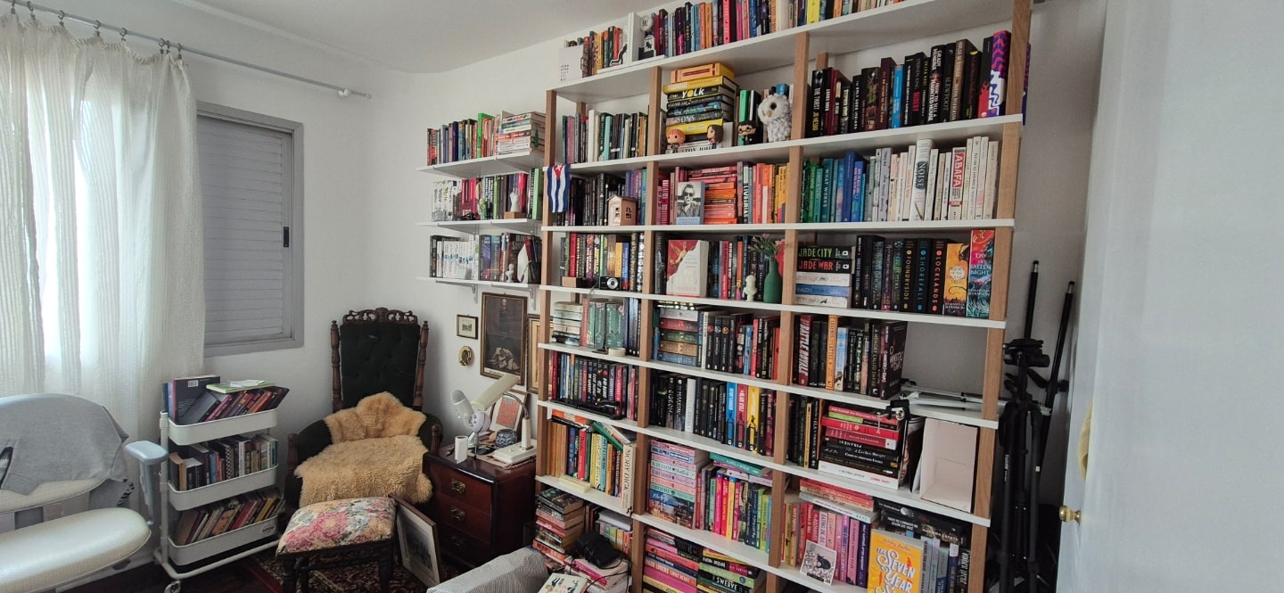 Estante repleta de livros e uma poltrona no canto do cômodo.