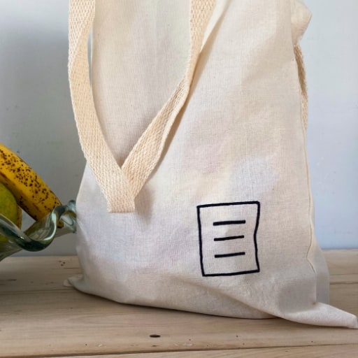 Sacola de tecido com o logo do Manual do Usuário em cima de uma mesa de madeira.