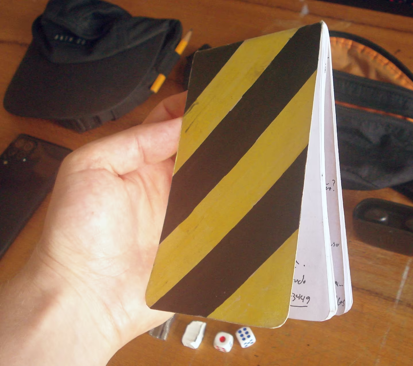 Mão segurando caderninho com espiral em cima e capa com listras amarelas e marrons.