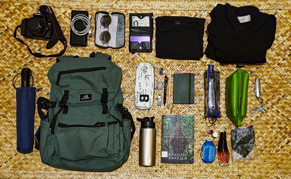Itens da mochila da Daniely dispostos em uma superfície de palha trançada.