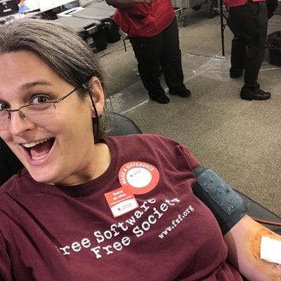 Mulher branca, de óculos, sentada e vestindo uma camiseta de software livre.