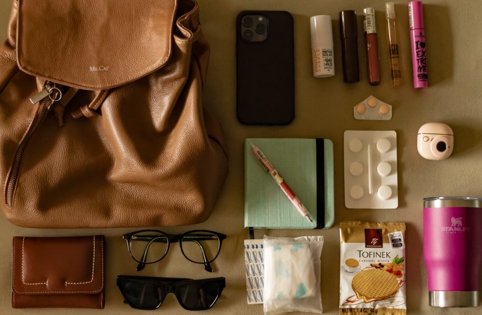 Foto de uma bolsa e vários itens, de uma perspectiva de cima.