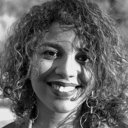 Foto em preto e branco de mulher com cabelos cacheados, sorrindo.