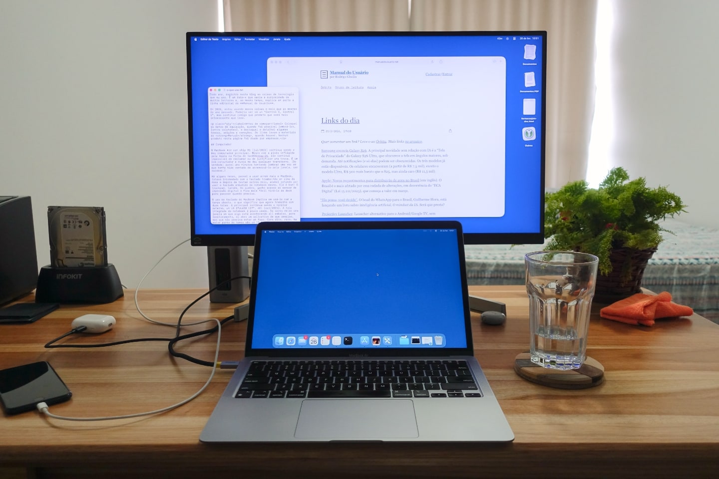 Foto frontal de uma mesa de trabalho, com um monitor e um notebook aberto e alguns acessórios nas laterais.