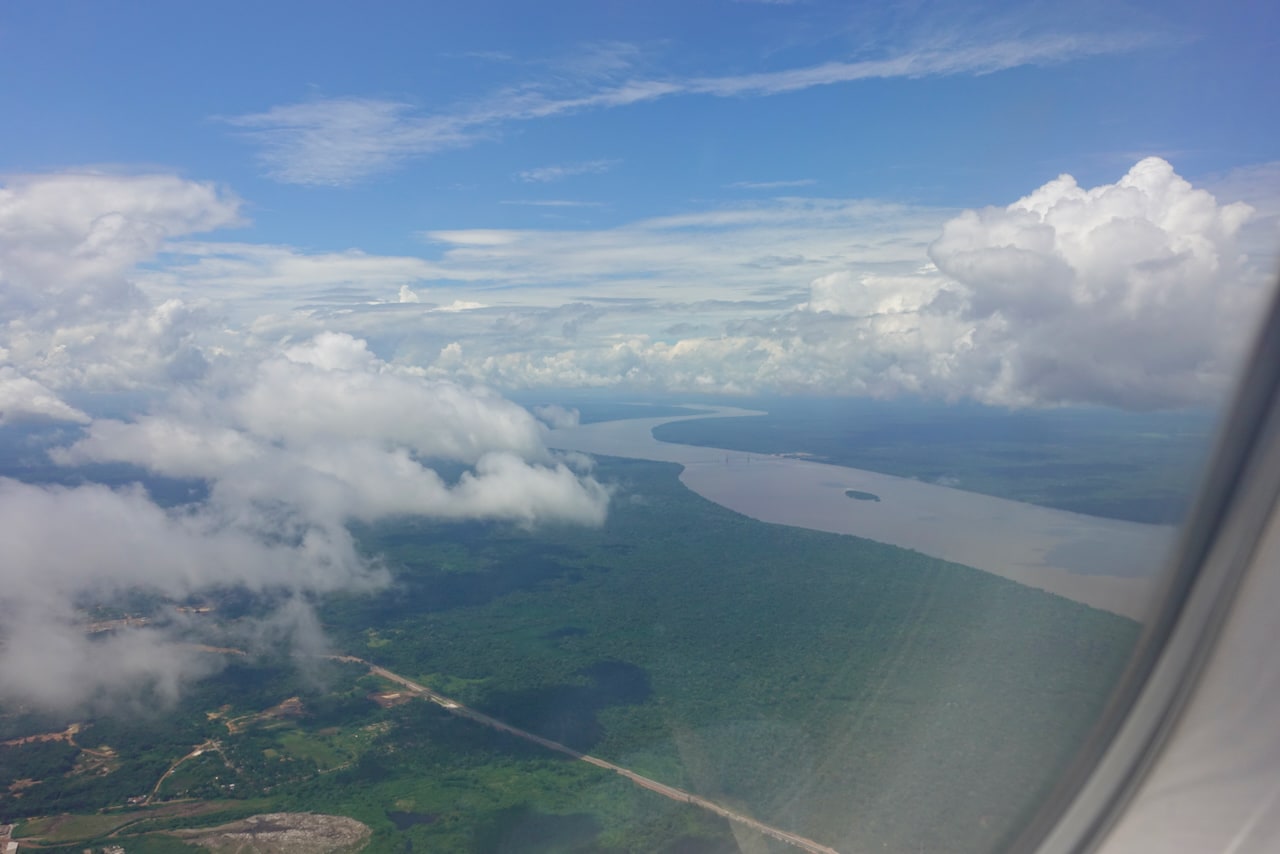 Aerial view from a plane window of part of the forest and a river, covered by some clouds.