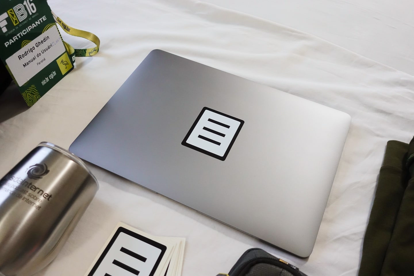 Detalhe de um MacBook Air (M1) com um adesivo do logo do Manual do Usuário sobre o logo da Apple.