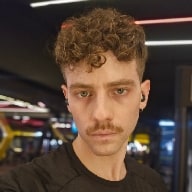 Homem branco, sério, de cabelo curto encaracolado e bigode.