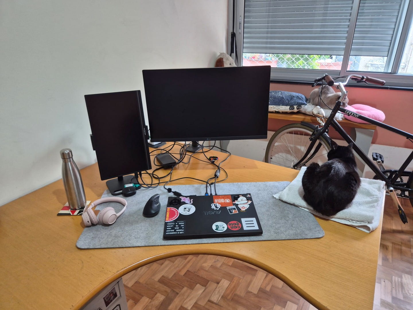 Mesa de trabalho do Pedro por outro ângulo, com notebook fechado e monitores desligados.