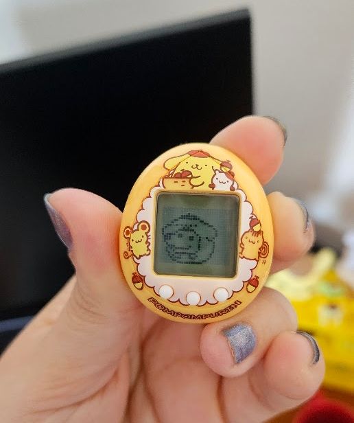 Tamagotchi in a yellow box being held in a hand.
