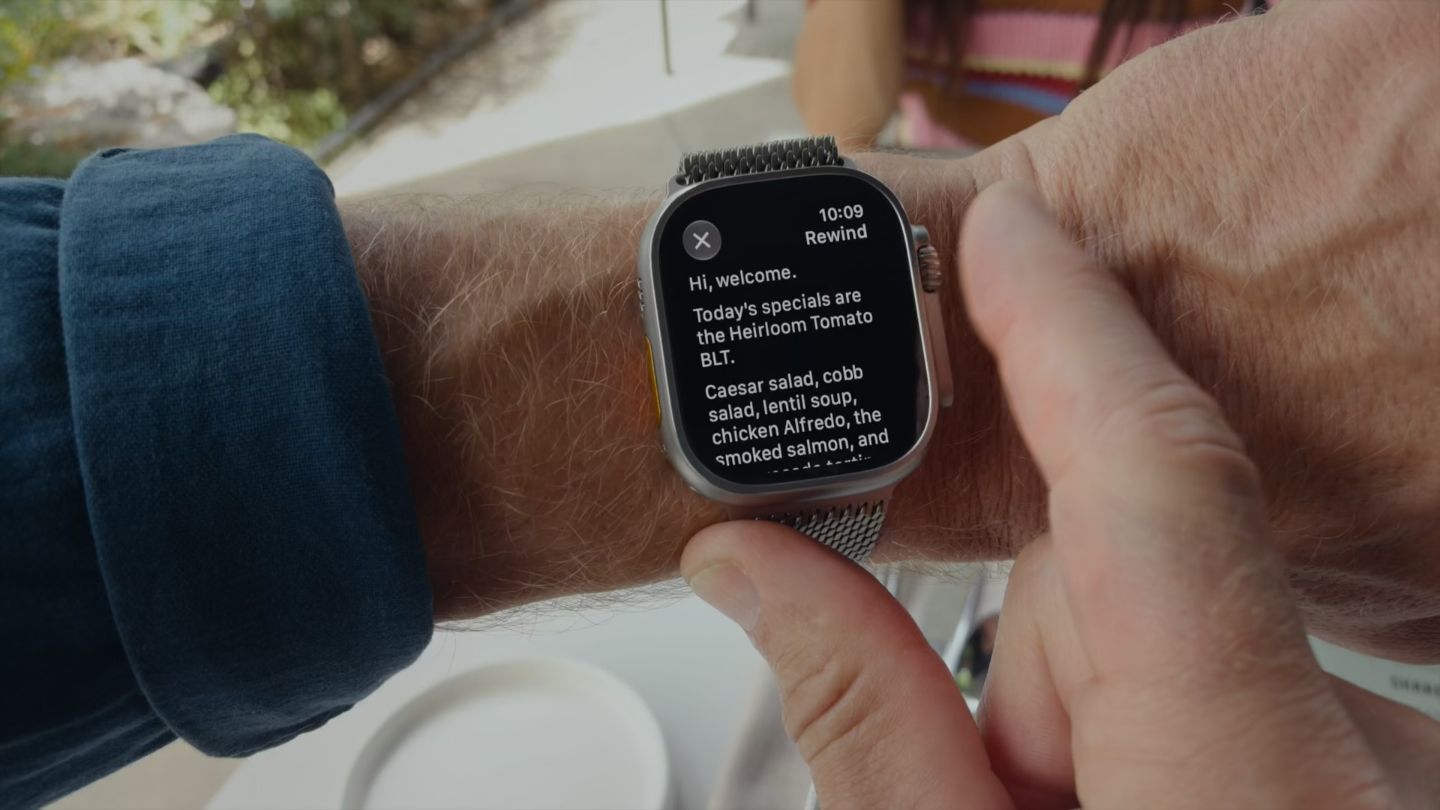 Foto de um Apple Watch Ultra 4 no braço de alguém, mostrando a transcrição de uma conversa recente captada pelo recurso Live Rewind.